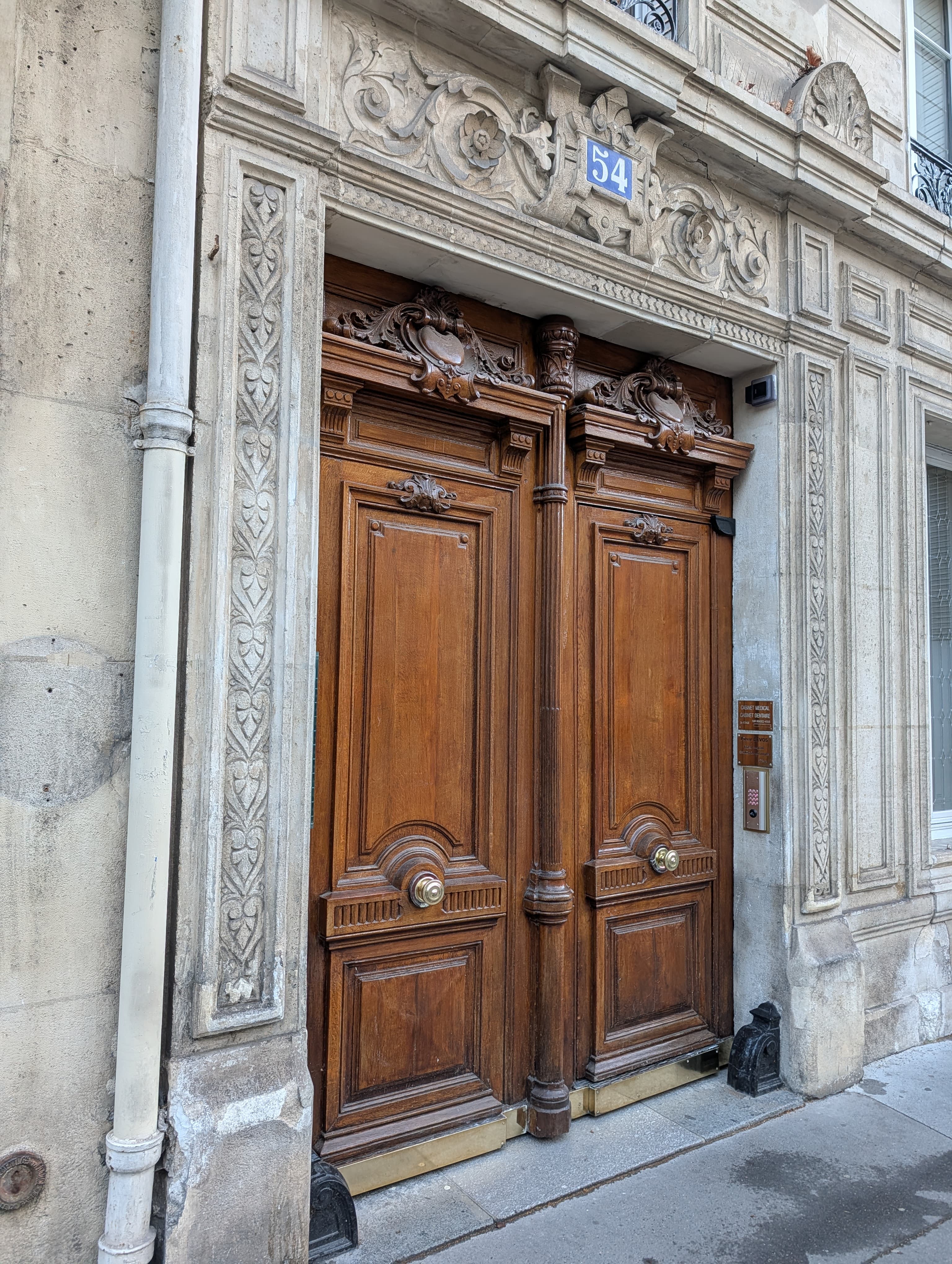 Porte double en bois sculpté sous une arche en pierre ornée au numéro 54.